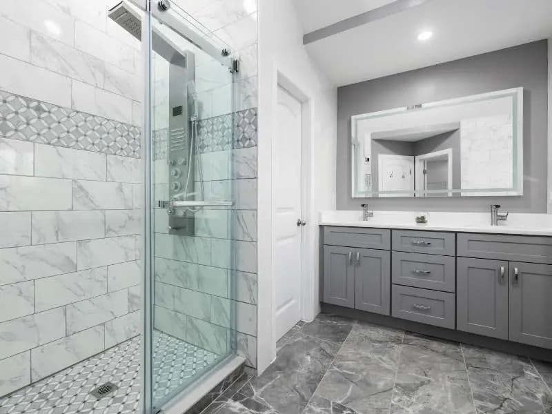 Modern bathroom featuring glass shower, marble tiles, gray cabinetry, and large mirror.