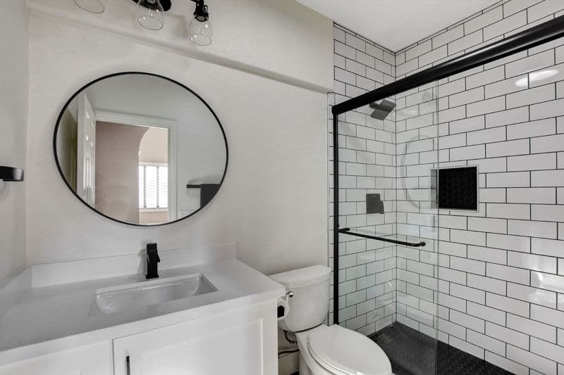 Modern bathroom featuring a round mirror, sleek vanity, and glass shower with white subway tiles.