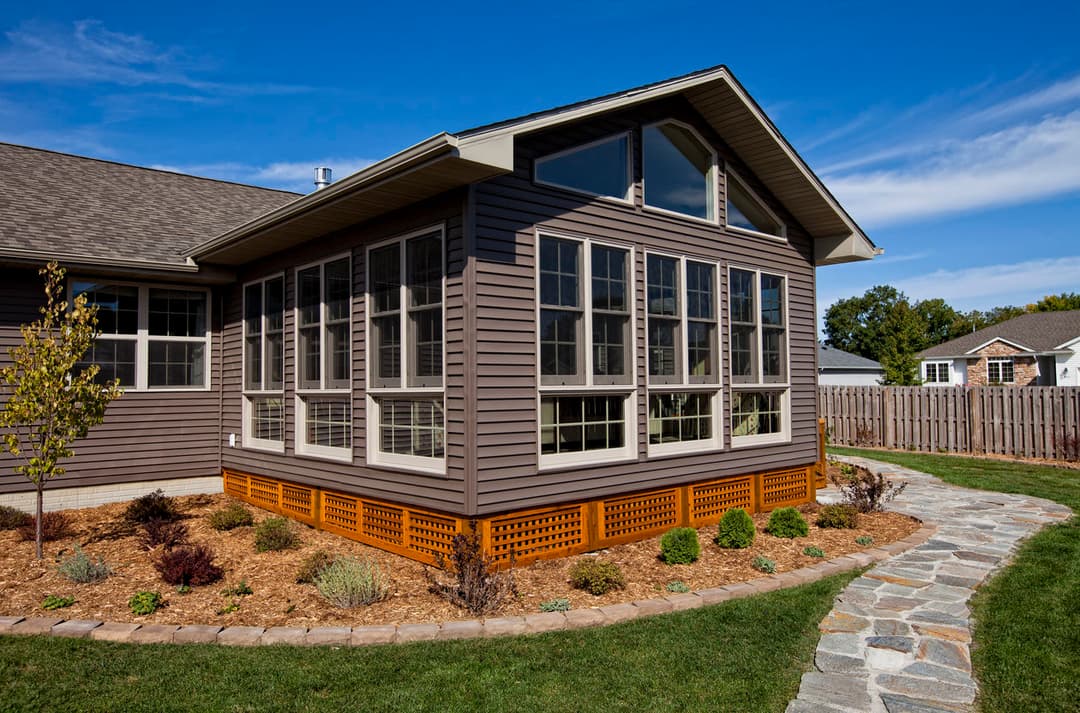 Modern gray sunroom with large windows, stone pathway, and landscaped yard.
