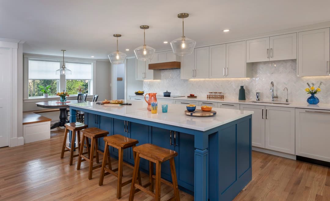 Modern kitchen with blue island, white cabinets, and elegant lighting fixtures. Cozy dining area.