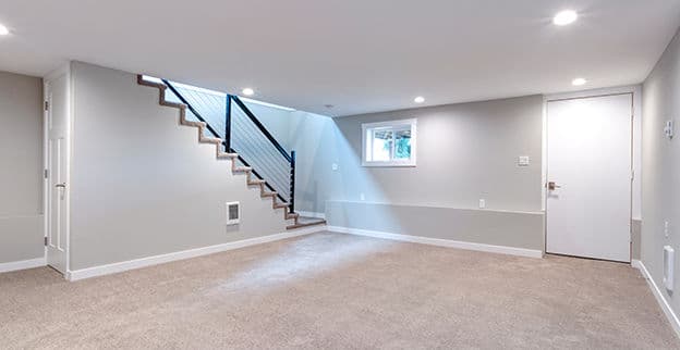 Modern empty basement with staircase, window, and neutral gray walls. Ideal for renovation.