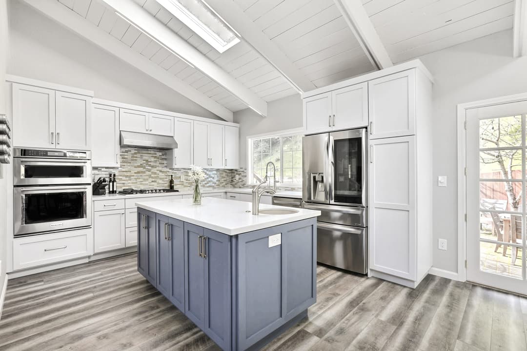 Modern kitchen with white cabinets, blue island, stainless steel appliances, and natural light.